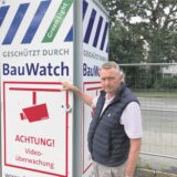 Ein düster dreinblickender Mann zeigt auf ein Schild, das eine Videoüberwachung anzeigt