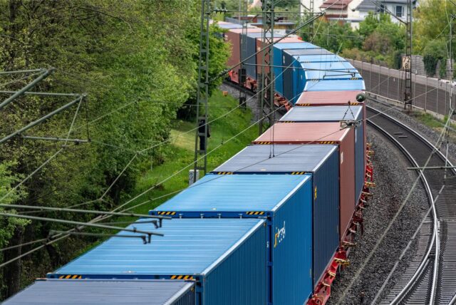 Ein Güterzug mit vielen Containern fährt über Bahnschienen.