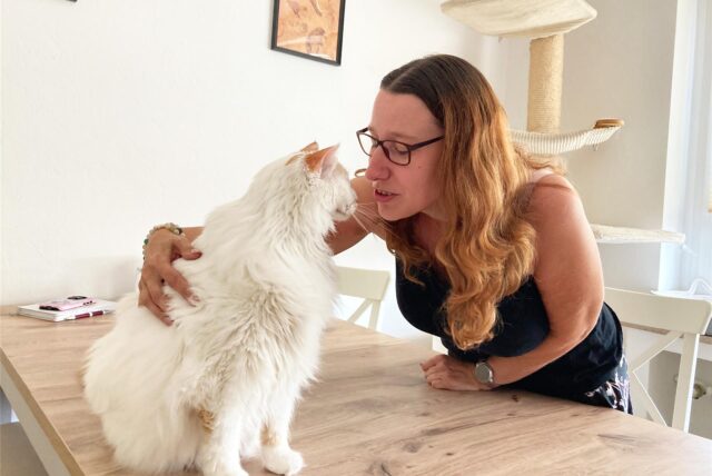 Michaela Weinkauf beugt sich zu ihrer Katze Mayo, die auf dem Tisch sitzt, und streichelt sie.