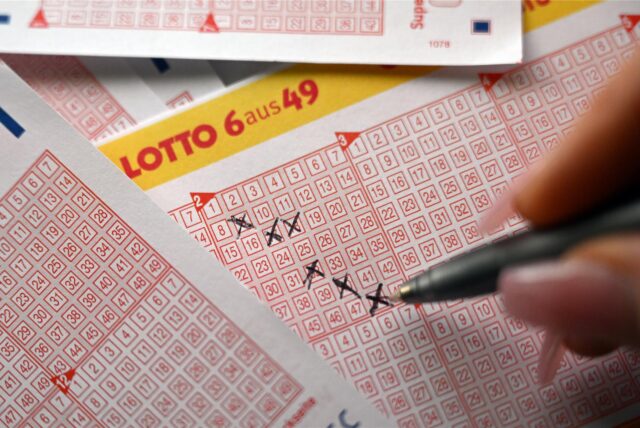 Lotto 6 aus 49 – eine Hand mit rosa Fingernägeln kreuzt auf einem Tippschein mögliche Gewinnzahlen an.