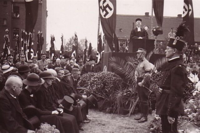 Hakenkreuzfahnen säumen die Trauerfeier für die verunglückten Bergleute 1935 in Mengede. An einem Rednerpult steht Dr. Albrecht Stenger, seinerzeit Pfarrer der evangelischen Remigiusgemeinde.