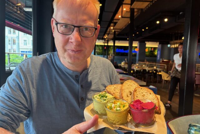 Reporter Markus Geling sitzt bei WIlma Wunder in Recklinghausen und hält einen Teller mit Brot und Dips.