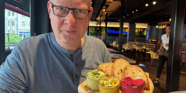 Reporter Markus Geling sitzt bei WIlma Wunder in Recklinghausen und hält einen Teller mit Brot und Dips.