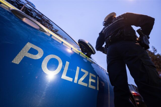 Ein Polizist steht vor einem Streifenwagen.