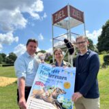 Rajko Krawanja, Julia Schulze und Jens Langensiepen mit dem Plakat zum Castroper Pferderennen 2025 und einem Steckenpferd.