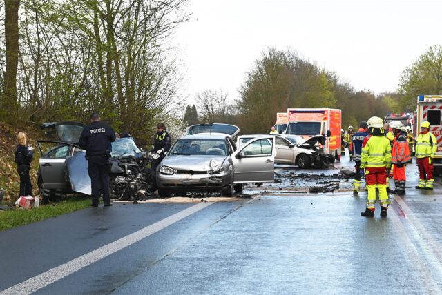 Das Bild vom Unfall damals: Drei beschädigte Autos stehen auf der Straße, umgeben von Polizisten und Rettungskräften.