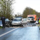 Das Bild vom Unfall damals: Drei beschädigte Autos stehen auf der Straße, umgeben von Polizisten und Rettungskräften.