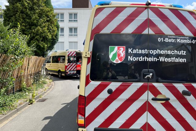 Ein Einsatzfahrzeug des Katastrophenschutzes Nordrhein-Westfalen steht auf einer Straße. Der geöffnete Transporter des Deutschen Roten Kreuzes ist im Hintergrund zu sehen.