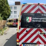 Ein Einsatzfahrzeug des Katastrophenschutzes Nordrhein-Westfalen steht auf einer Straße. Der geöffnete Transporter des Deutschen Roten Kreuzes ist im Hintergrund zu sehen.