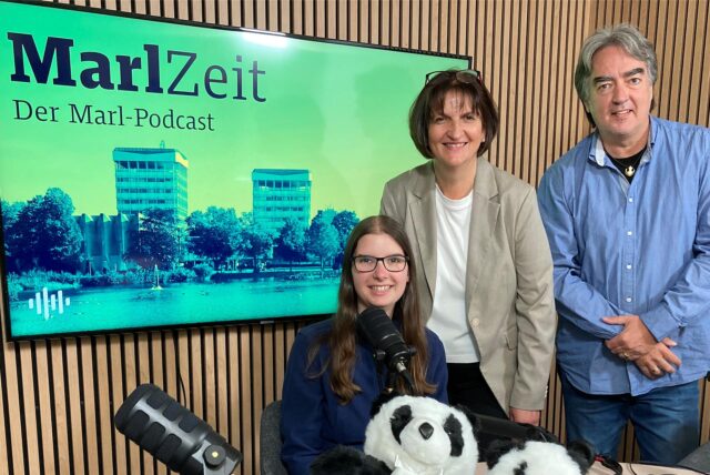 Katharina Göke (l.), Martina Möller und Patrick Köllner vor einem Bildschirm, auf dem auf den Podcast „MarlZeit“ hingewiesen wird.