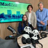 Katharina Göke (l.), Martina Möller und Patrick Köllner vor einem Bildschirm, auf dem auf den Podcast „MarlZeit“ hingewiesen wird.