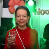 Lara Linka steht mit einem Glas in der Hand vor dem DJ-Pult.