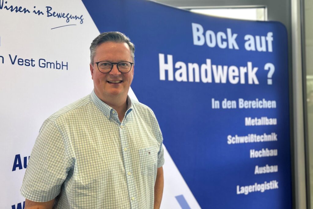 Ein Mann steht vor einem Werbebanner, das für handwerkliche Berufe wirbt. Das Banner wirbt mit der Frage 