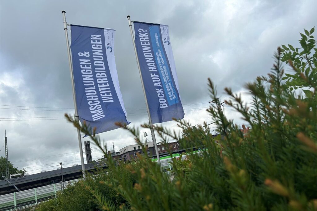 Zwei Werbefahnen des Schulungs- und Servicezentrum Vest GmbH stehen im Freien. Die Fahnen werben für Umschulungen und Weiterbildungen sowie Handwerksberufe.