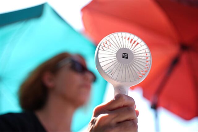Eine Frau kühlt sich mit einem Handventilator unter Sonnenschirmen auf einem Balkon in der Mittagssonne ab. Die Hitzewelle in Deutschland sorgt auch im Norden für schweißtreibende Temperaturen.