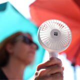 Eine Frau kühlt sich mit einem Handventilator unter Sonnenschirmen auf einem Balkon in der Mittagssonne ab. Die Hitzewelle in Deutschland sorgt auch im Norden für schweißtreibende Temperaturen.