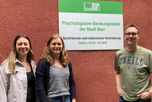 Selina Kemper, Annika Fricke und Marco Timmerhinrich stehen vor einem Schild der Psychologischen Beratungsstelle der Stadt Marl.