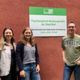 Selina Kemper, Annika Fricke und Marco Timmerhinrich stehen vor einem Schild der Psychologischen Beratungsstelle der Stadt Marl.