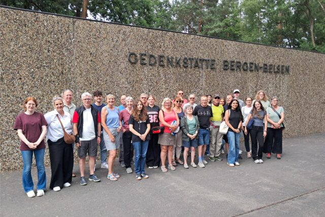 Gruppe von Teilnehmenden der „Tour de Demokratie“ steht vor der Wand mit dem Schriftzug „Gedenkstätte Bergen-Belsen“.