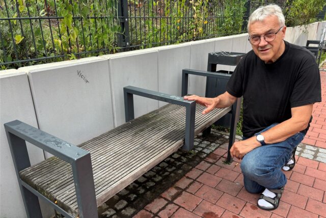 Gastkirchen-Pfarrer Ludger Ernsting kniet neben einer Bank mit Mittellehne in der Sterngasse in der Altstadt von Recklinghausen.