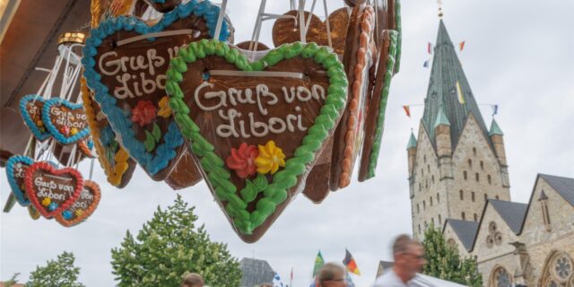 Lebkuchenherzen mit der Aufschrift „Gruß von Libori“ hängen an einem Stand der Libori-Kirmes in Paderborn. Im Hintergrund sind Besucher und der Dom zu sehen.