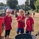 Drei Kinder in roten T-Shirts auf einem Sportplatz
