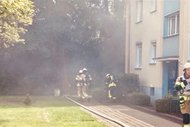 Rauch dringt aus einem Mehrfamilienhaus an der Wasserbank in Recklinghausen. Vor dem Gebäude sind Feuerwehrkräfte zu sehen.