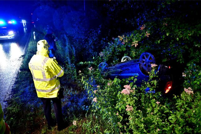 An der Röllinghauser Straße liegt ein Auto nach einem Unfall im Graben, davor steht ein Polizist